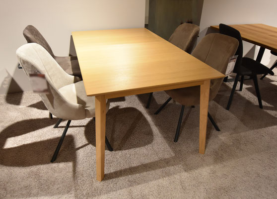 Heller Holztisch und vier verschiedene Esszimmerstühle auf beigem Teppichboden.