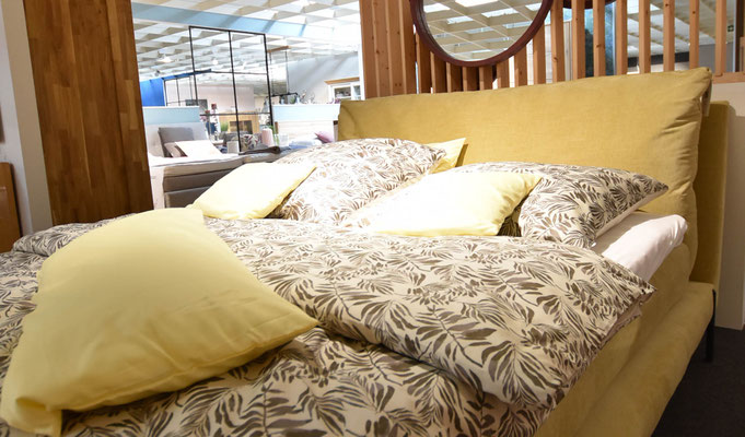 Großes, gelbes Bett mit floral gemusterter Bettwäsche und gelben Kissen in der Möbel-Ausstellung.