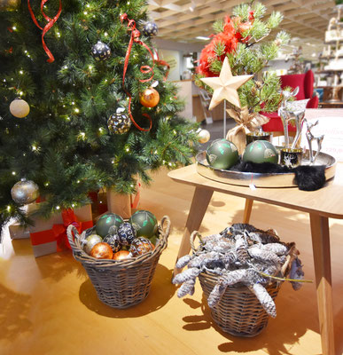 Weihnachtsbaum mit Lichtern und Kugeln. Im Hintergrund, ein weiterer Baum und rote Polstermöbel.