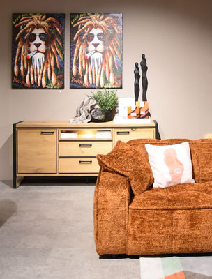 Orangefarbenes Sofa vor einem Sideboard aus Eichenholz und zwei Bildern mit einem Löwen.