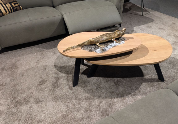 Zwei ovale Eichenholz-Couchtische mit einem goldenen Krokodil auf Kunstfell, vor einem Sofa.