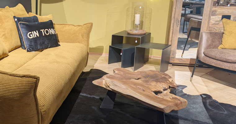 Gelbes Cordsofa mit schwarzem "GIN TONIC"-Kissen, rustikalem Couchtisch auf Kuhfell-Teppich.