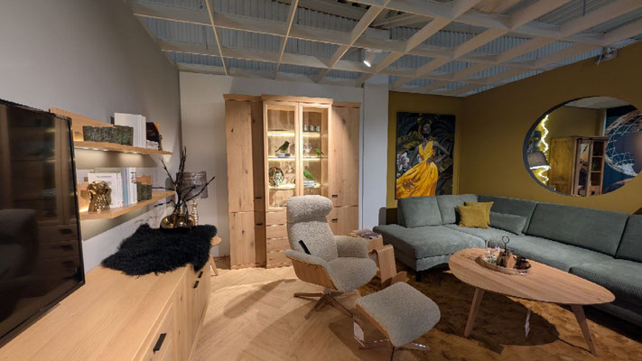 Helles Wohnzimmer mit Sofa, beigem Sessel, Couchtisch und Holzschränken. Großer Spiegel an der Wand.