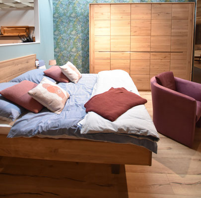 Modernes Schlafzimmer mit Holzschrank, Holzbett, blauer Bettwäsche und einem Sessel.