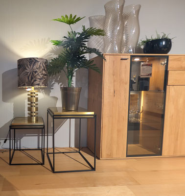 Zwei schwarze Metall-Beistelltische mit Messingakzenten und einer Lampe, daneben ein Holzschrank.