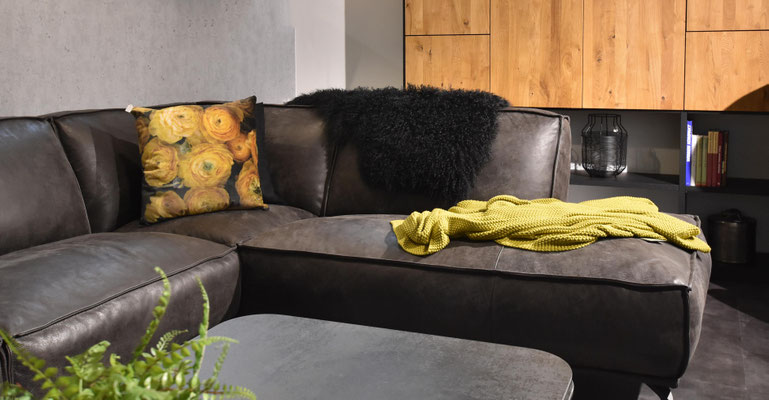 Nahaufnahme eines braunen Ledersofas mit zweifarbigen Kissen und einer gelben Decke.