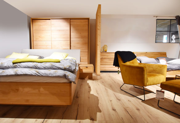 Großes Schlafzimmer mit Holzboden, gelbem Sessel, zwei Holzbetten und Schiebetürenschrank.