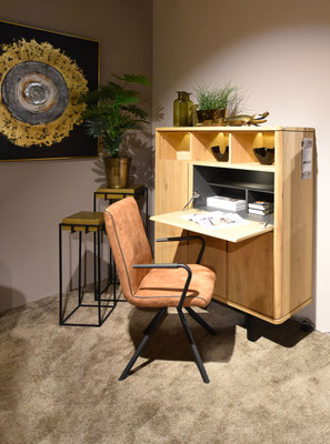 Schreibtisch-Sekretär aus hellem Holz, dazu ein brauner Stuhl und goldene Deko in einer Ecke.