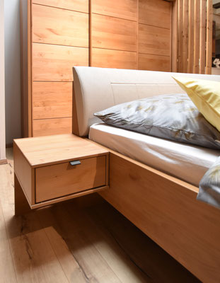 Modernes Bett in hellbraunem Holz und weißem Kopfteil mit gelbem Kissen und einem Holznachttisch.