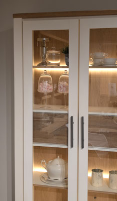 Weißer Schrank mit Glastüren, Holzfächern und beleuchteten Dekorationen.