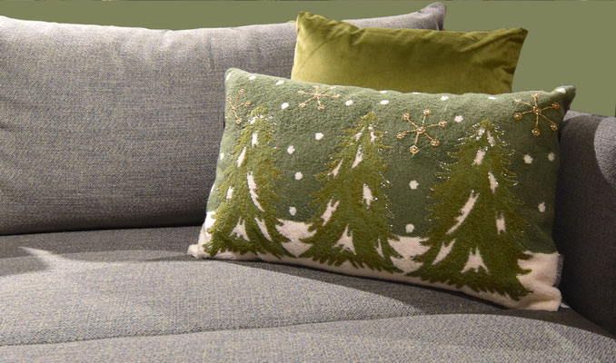Grünes Kissen mit Stickerei auf einem grauen Sofa neben einem olivgrünen Kissen.