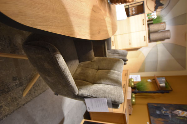 Gesteppter Armlehnstuhl mit olivgrünem Bezug und Holztisch, im Hintergrund ein Holzschrank.