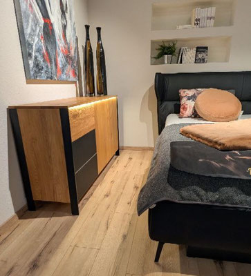 Modernes Schlafzimmer mit schwarzem Lederbett, hell beleuchtetem Sideboard und Kunst.