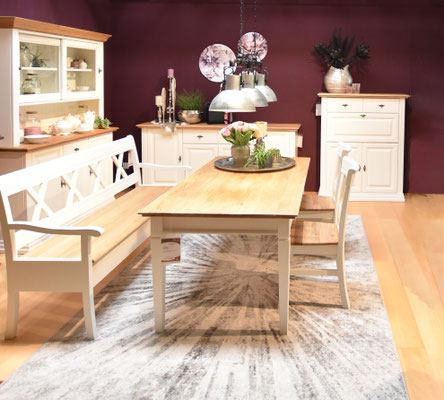 Weißer Tisch mit Holzplatte, Sitzbank und Vitrine vor weinroter Wand im Esszimmer.