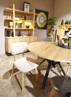 Runder Holztisch und beiger Stuhl vor einem beleuchteten Holzregal in modernem Raum.