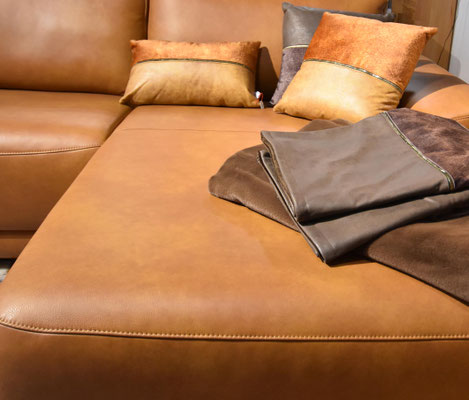  Nahaufnahme einer karamellbraunen Ledercouch mit kontrastierenden Kissen und einer braunen Decke.