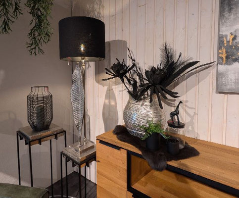 Eleganter Innenraum mit Stehlampe, Metallvase mit schwarzen Federn und Holzkabinett.