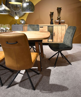 Zwei moderne Stühle, einer senfbraun, der andere dunkelgrün, an einem ovalen Esstisch in einem Speisezimmer.