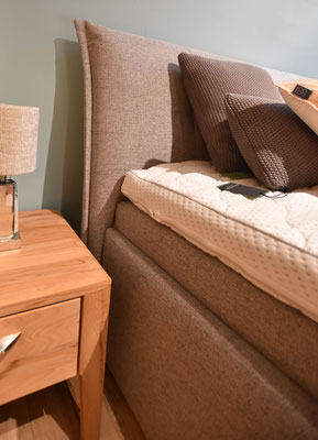 Boxspringbett: Basis in Braungrau, hellgrauer Matratze, weißer Topper und Kissen auf Holzboden.