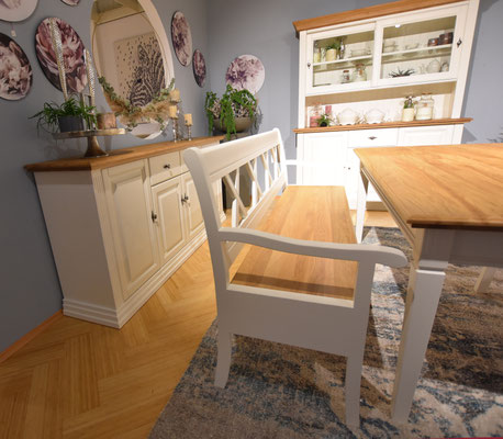 Esszimmer mit Holztisch, weißer Bank und Stühlen, weißem Geschirrschrank und Sideboard.