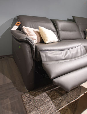 Dunkelgraues Ledersofa mit integrierter Fußstütze und zwei hellen Zierkissen.