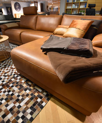 Cognacfarbenes Ledersofa (Chaise Lounge) mit Decken und kariertem Fellteppich.