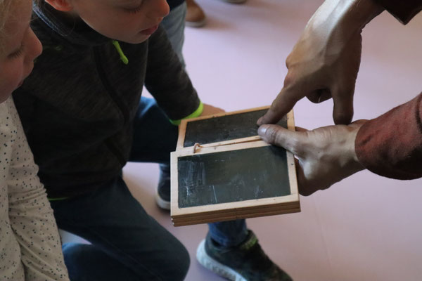 Les élèves voient au plus près des reproductions d'objets de l'époque, ici l'ancêtre de leur ardoise : une tablette de cire.