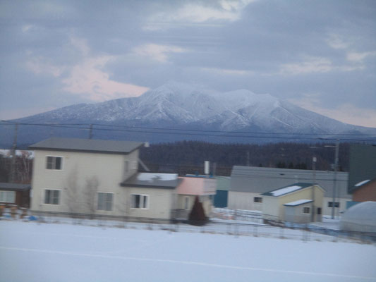 川湯温泉を過ぎ、緑駅から札弦（さっつる）に入る頃　右手（東側）に斜里岳が見えてくる！　北海道の日暮れは早いので、かろうじて白い山容が見えるだけだったが、感動ひとしお…