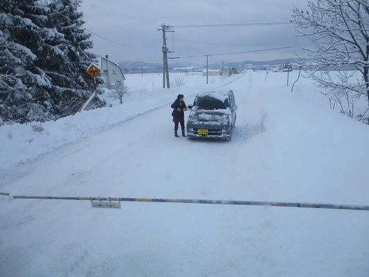 踏切で停車している車　後続車もおらず、運転手の女性は降りてフロントの除雪をして待っている