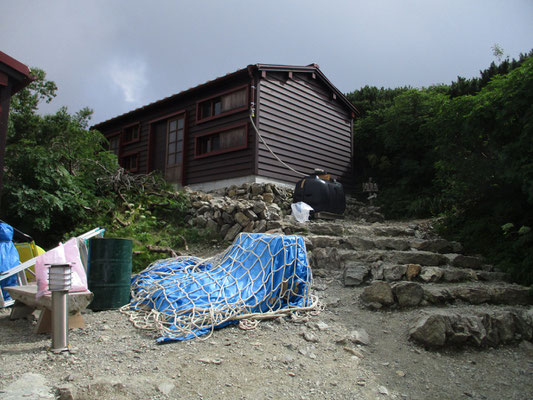 ハイマツの裏に上手いこと塩見小屋がありました　厳しい立地条件のこの小屋は大きくありません　そしてトイレは携帯トイレ利用で汚物はまとめてヘリで下ろすシステムです　山では排泄物問題が水の確保と同じく最重要課題