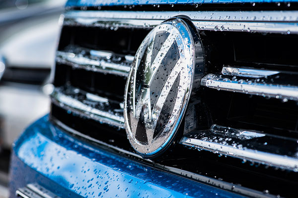 Detailansicht eines VW Logos am Kühlergrill eines mittelblauen Fahrzeuges