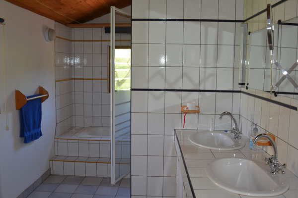 Badkamer met bad, aparte douche en dubbele wastafel.