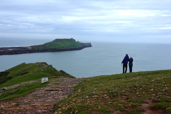 Zwei Wanderer betrachten die Gezeiteninsel Worm's Head in Wales