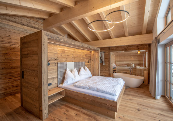 Holzgetäfeltes Schlafzimmer mit Doppelbett, freistehender Badewanne und großen Fenstern
