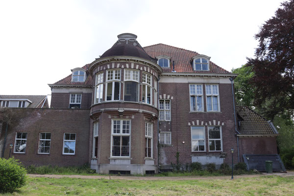 De achtergevel van het huis heeft een samengestelde plattegrond. Ter plekke van de gesloten eenlaags aanbouw stond oorspronkelijk een serre, vanwaar men vanuit het huis de tuin kon betreden. 