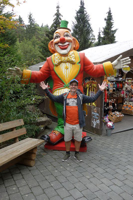 Andreas posiert lachend vor einer großen, bunten Clown-Figur im Parkgelände