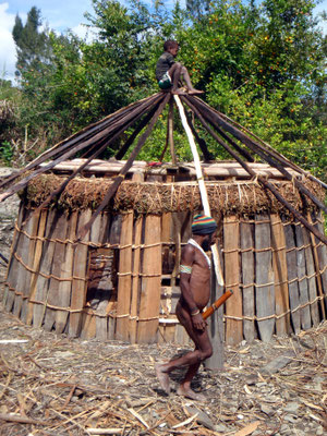 Papua in traditioneller Kleidung vor einer Frauenhütte