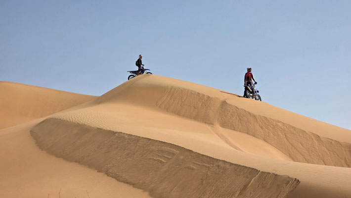 TWO ENDURO RIDERS ON THE RIDGE OF A LARGE SAND DUNE IN THE RUB AL KHALI, OMAN