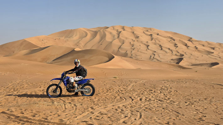 PILOTE D’ENDURO SUR UNE PLAINE DE SABLE DANS LE RUB AL KHALI, GRANDES DUNES EN ARRIÈRE-PLAN