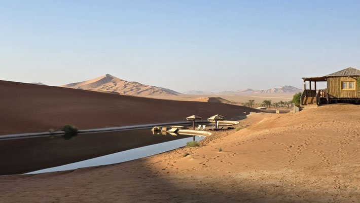 WASSERBECKEN IN DER WÜSTE MIT CAMP UND DÜNEN IM HINTERGRUND