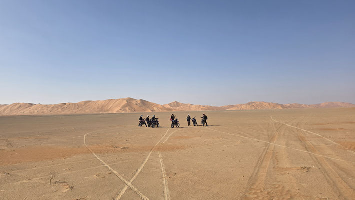 GROUPE D’ENDURO SUR UNE VASTE PLAINE DANS LE DÉSERT AVEC DES TRACES DANS LE SABLE