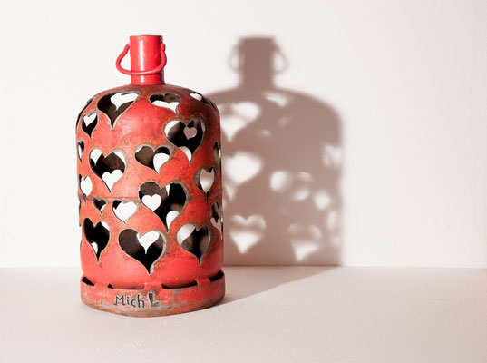 Sculpture en acier réalisée à partir d'une bouteille de gaz rouge, percée de coeurs