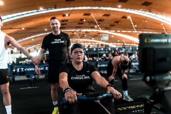 Sabine Bell (Bine) rudert am RowErg bei HYROX Karlsruhe 2025, Trainer Christoph Wieloch steht dahinter und unterstützt.