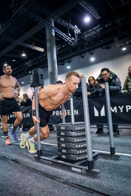 Christoph Wieloch beim Sled Push mit beladenem Schlitten bei HYROX Frankfurt, Zuschauer im Hintergrund.