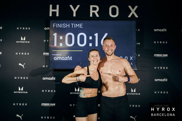 Christoph Wieloch und Inga de Busman posieren nach dem Wettkampf vor der Anzeige mit ihrer Zielzeit beim HYROX Event in Barcelona.