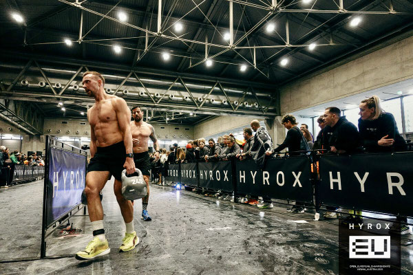 Christoph Wieloch beim Farmers Carry (Kettlebell) bei HYROX Wien 2025, Zuschauer an der Strecke.