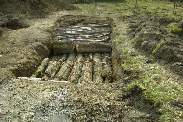 Die ausgehobene Grube wird mit Baumstämme und Äste aufgefüllt. 