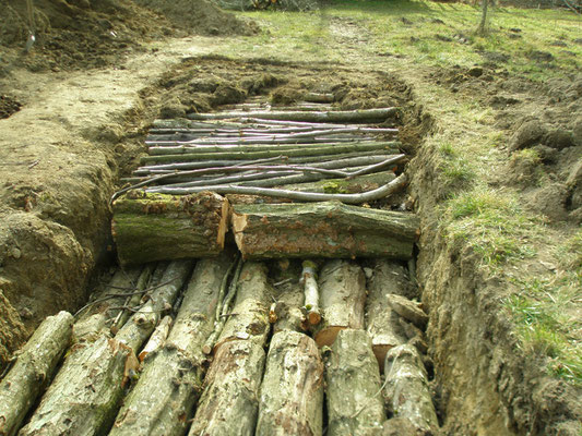 Die ausgehobene Grube wird mit Baumstämme und Äste aufgefüllt. 