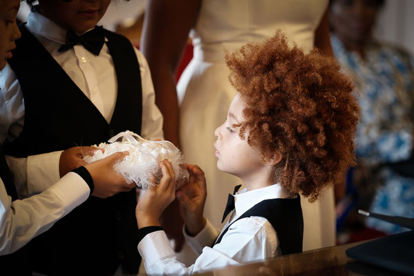 enfant blanc avec des tâches de rousseur et des cheveux roux et une coupe afro tient les alliances de ses parents