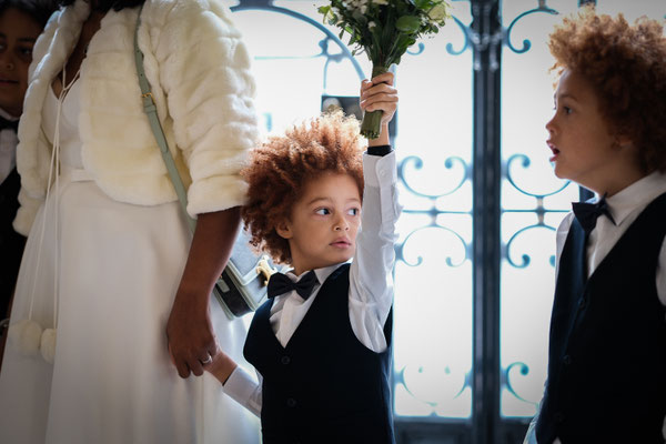 enfant blanc avec des tâches de rousseur et des cheveux roux et une coupe afro brandit le bouquet de mariée de sa mère